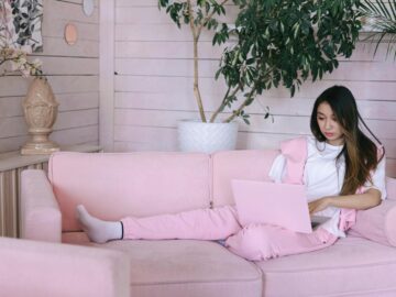Asian woman working on a laptop from a cozy pink couch in a stylish indoor setting.