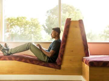 man sitting on red cushion beside window