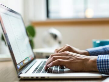 Close-up of adult typing on laptop in bright, modern office.
