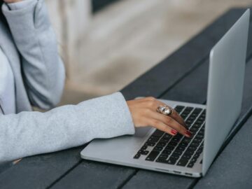 Side view of crop anonymous female entrepreneur in luxury ring working on netbook at wooden table