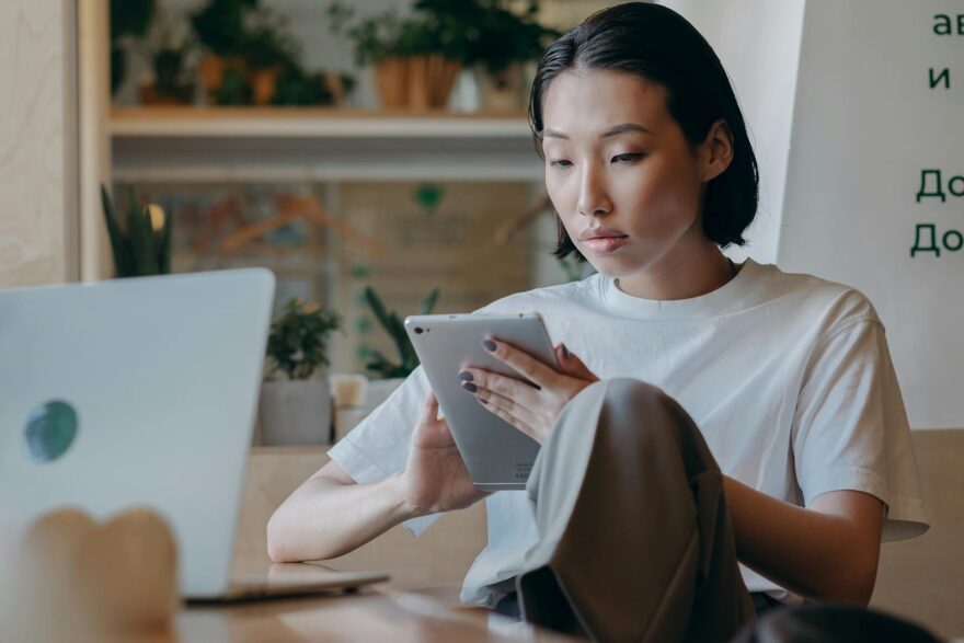Focused Asian businesswoman using a tablet in a modern, plant-filled workspace with natural lighting.